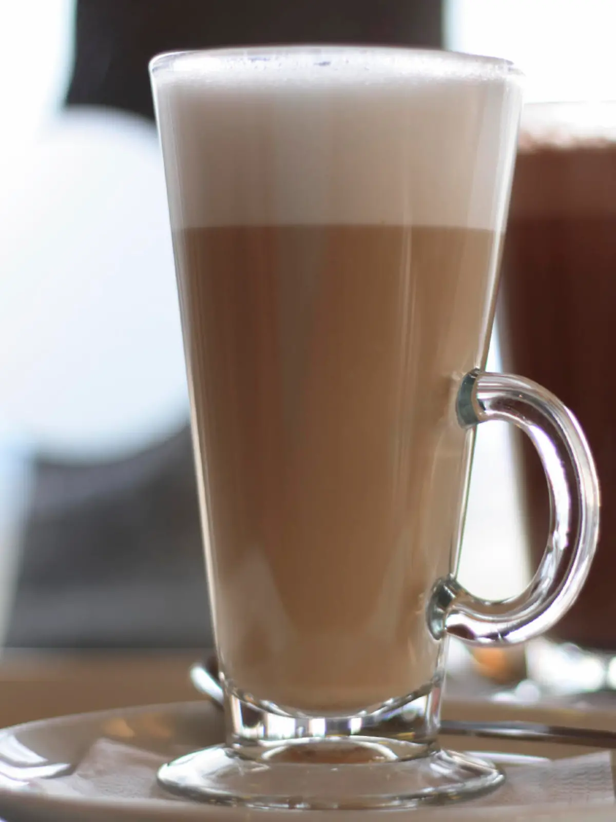Cafe Latte in a glass with hot chocolate in background
