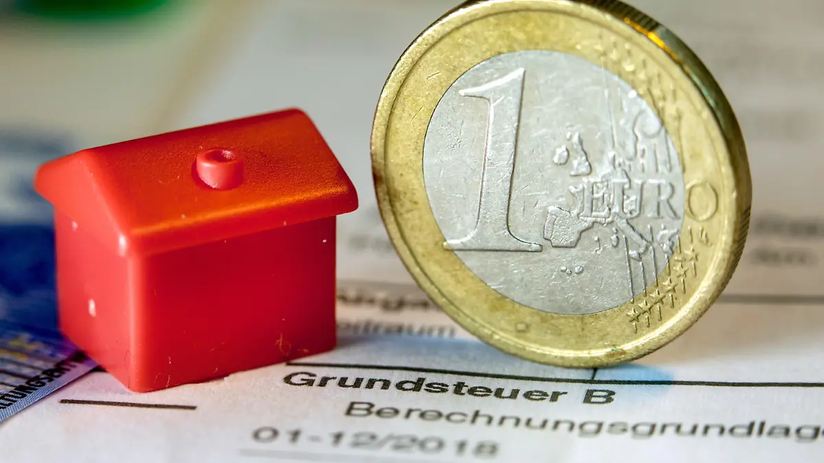 ARCHIV - 30.01.2019, Mecklenburg-Vorpommern, Schwerin: Illustration - Eine Euro-Geldmünze sowie ein Spielzeughaus stehen auf einem Abgabenbescheid für die Entrichtung der Grundsteuer. Im Saarland fehlen derzeit noch rund 64 000 Erklärungen für die neue Grundsteuer. Die Frist zur Abgabe der Erklärung zur Feststellung des Grundsteuerwerts war Ende Januar ausgelaufen. (zu dpa: «Ministerium: Es fehlen noch rund 64 000 Grundsteuererklärungen»). Foto: Jens Büttner/ZB/dpa +++ dpa-Bildfunk +++