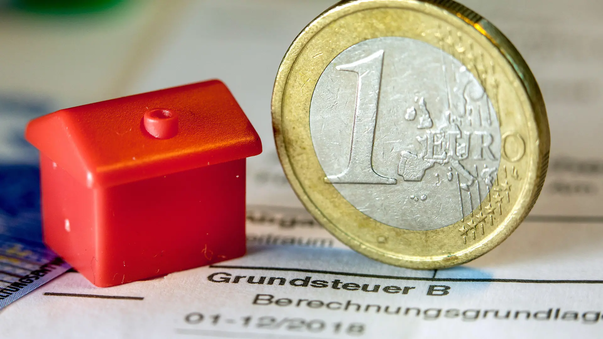 ARCHIV - 30.01.2019, Mecklenburg-Vorpommern, Schwerin: Illustration - Eine Euro-Geldmünze sowie ein Spielzeughaus stehen auf einem Abgabenbescheid für die Entrichtung der Grundsteuer. Im Saarland fehlen derzeit noch rund 64 000 Erklärungen für die neue Grundsteuer. Die Frist zur Abgabe der Erklärung zur Feststellung des Grundsteuerwerts war Ende Januar ausgelaufen. (zu dpa: «Ministerium: Es fehlen noch rund 64 000 Grundsteuererklärungen»). Foto: Jens Büttner/ZB/dpa +++ dpa-Bildfunk +++