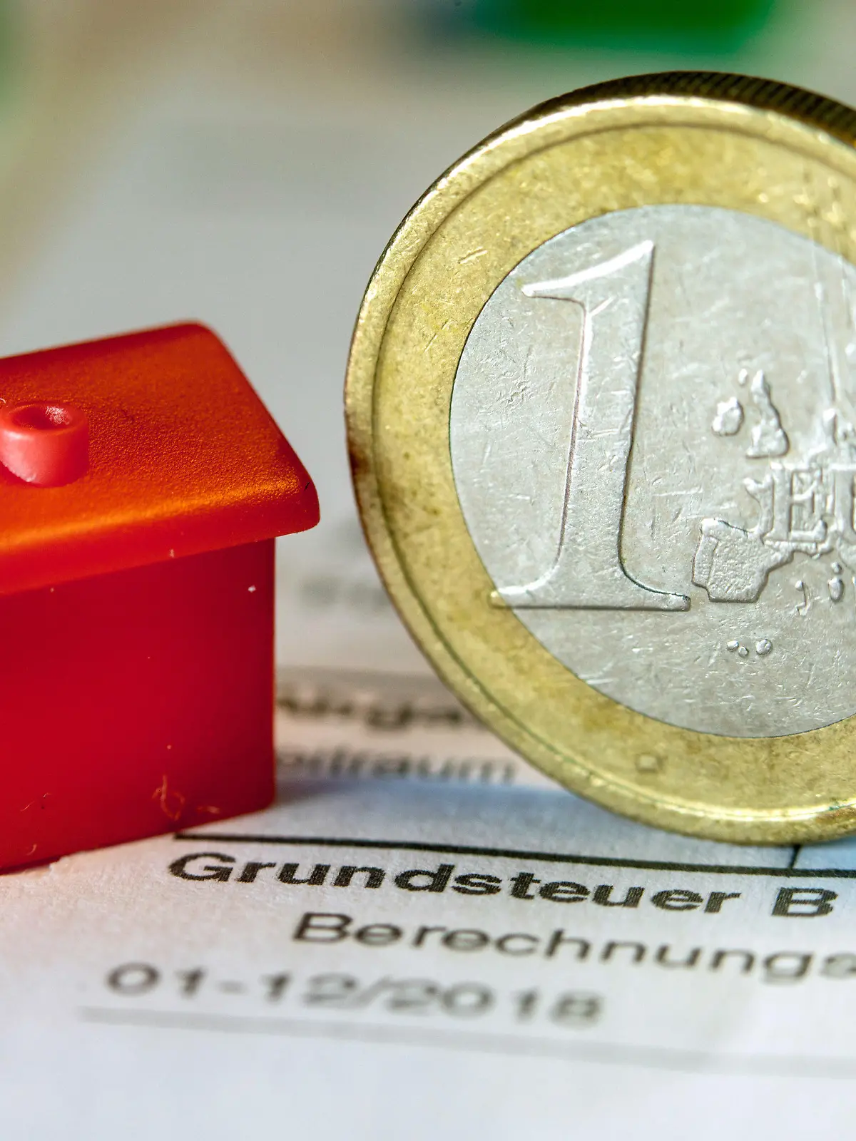 ARCHIV - 30.01.2019, Mecklenburg-Vorpommern, Schwerin: Illustration - Eine Euro-Geldmünze sowie ein Spielzeughaus stehen auf einem Abgabenbescheid für die Entrichtung der Grundsteuer. Im Saarland fehlen derzeit noch rund 64 000 Erklärungen für die neue Grundsteuer. Die Frist zur Abgabe der Erklärung zur Feststellung des Grundsteuerwerts war Ende Januar ausgelaufen. (zu dpa: «Ministerium: Es fehlen noch rund 64 000 Grundsteuererklärungen»). Foto: Jens Büttner/ZB/dpa +++ dpa-Bildfunk +++