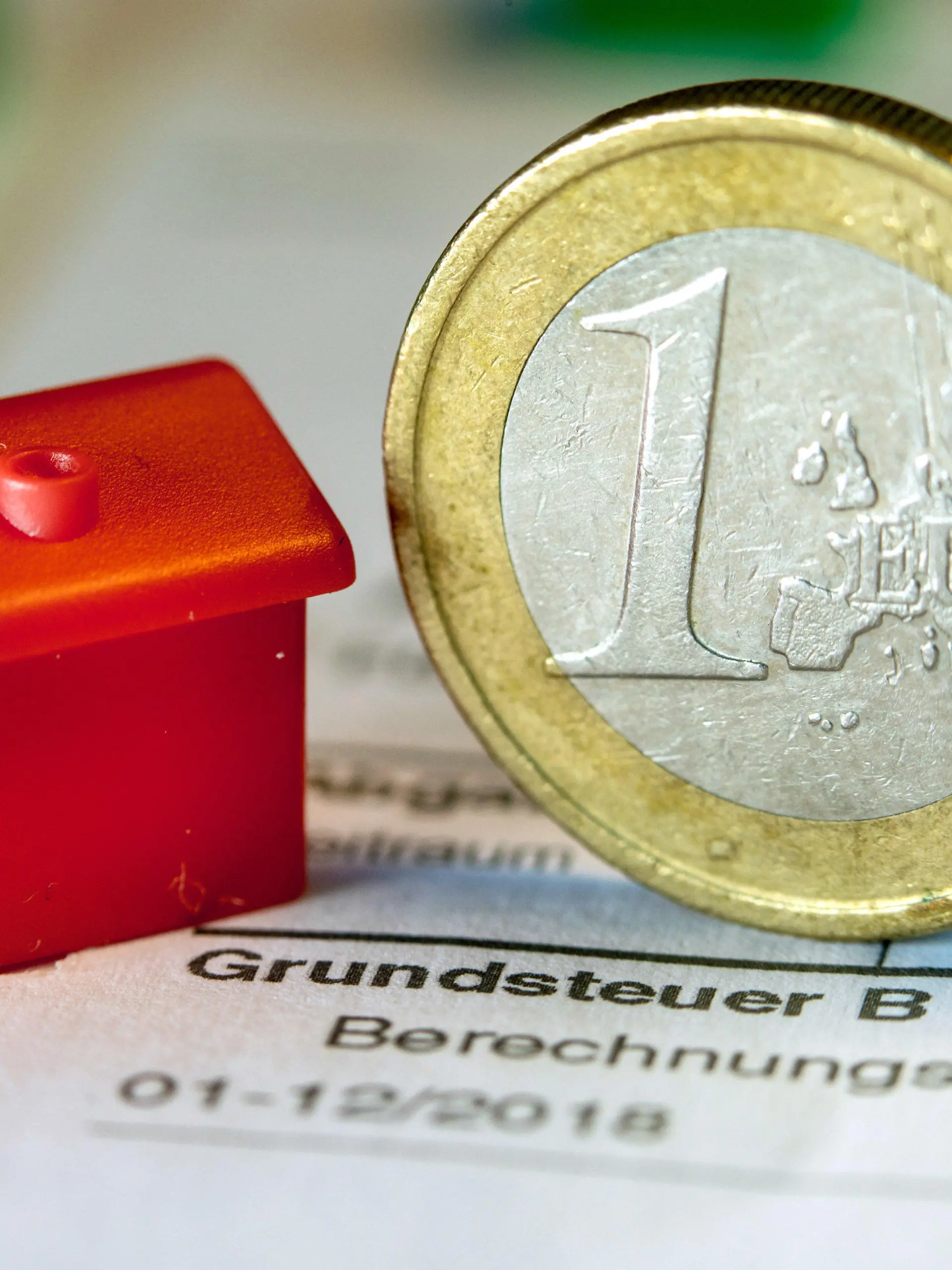 ARCHIV - 30.01.2019, Mecklenburg-Vorpommern, Schwerin: Illustration - Eine Euro-Geldmünze sowie ein Spielzeughaus stehen auf einem Abgabenbescheid für die Entrichtung der Grundsteuer. Im Saarland fehlen derzeit noch rund 64 000 Erklärungen für die neue Grundsteuer. Die Frist zur Abgabe der Erklärung zur Feststellung des Grundsteuerwerts war Ende Januar ausgelaufen. (zu dpa: «Ministerium: Es fehlen noch rund 64 000 Grundsteuererklärungen»). Foto: Jens Büttner/ZB/dpa +++ dpa-Bildfunk +++