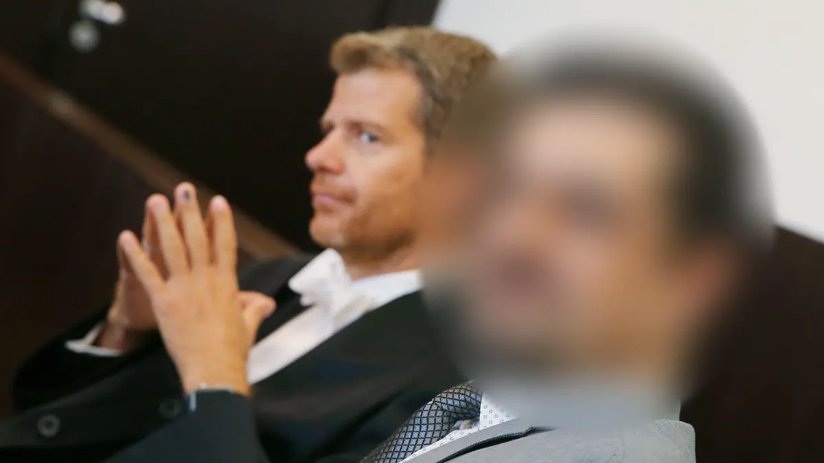 02.08.2019, Nordrhein-Westfalen, Düsseldorf: Anwalt Robert W. Kubach (l) und der Angeklagte sitzen zu Beginn des Prozesses im Gerichtssaal. Der Düsseldorfer Arzt, gegen den nach einer Po-Vergrößerung wegen fahrlässiger Tötung ermittelt wird, muss sich am 2. August 2019 in einer anderen Sache vor Gericht verantworten: Der 47-Jährige hat sich laut Anklage auf seiner Praxis-Homepage und in sozialen Netzwerken als «Dr. med.» ausgegeben, obwohl er nicht promoviert hat und daher keinen Doktortitel besitzt. Foto: David Young/dpa - ACHTUNG: Der Angeklagte wurde aus rechtlichen Gründen gepixelt +++ dpa-Bildfunk +++