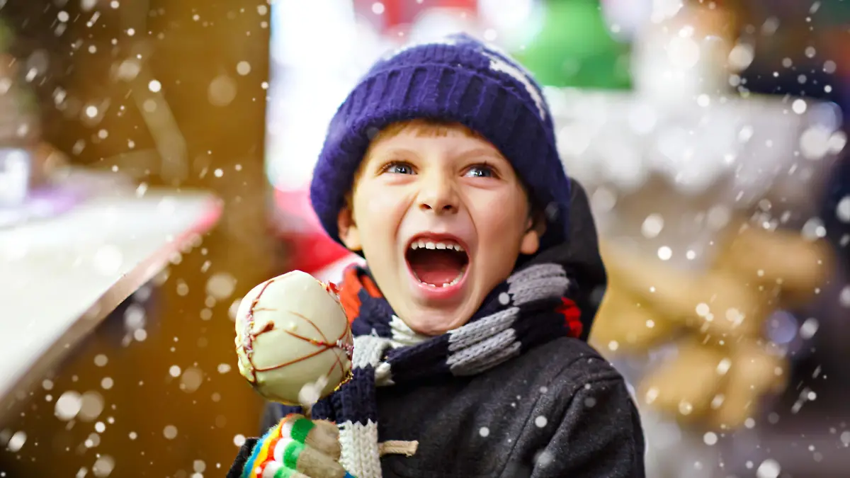 Little cute kid boy eating sugar apple near sweet stand with gingerbread and nuts. Happy child on Christmas market in Germany. Traditional leisure on xmas. Holiday, celebration, childhood.