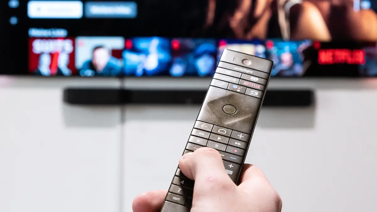 Ein Mann hält in seiner Wohnung eine Fernbedienung vor seinen Fernseher.
