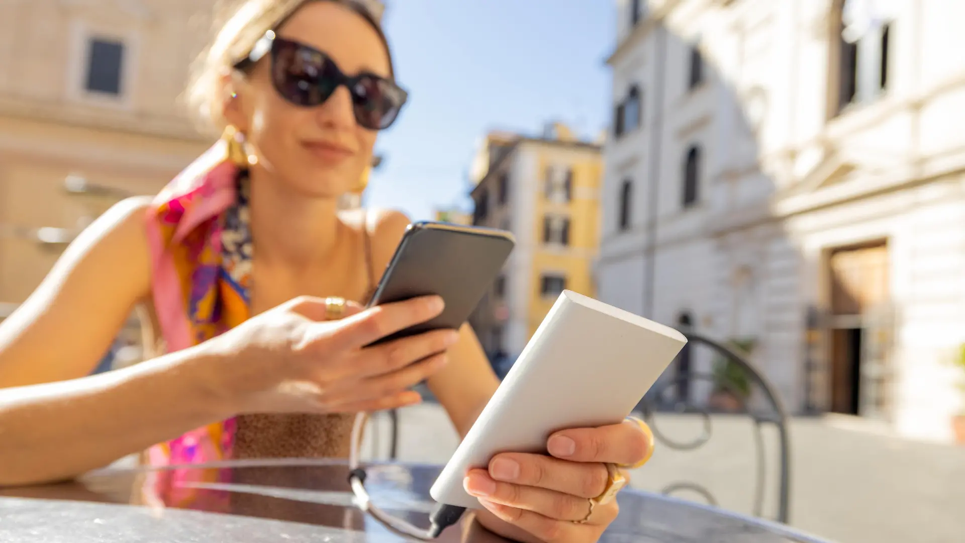 Woman charging phone with a power bank while sitting at cafe outdoors. Concept of charging gadgets for travel