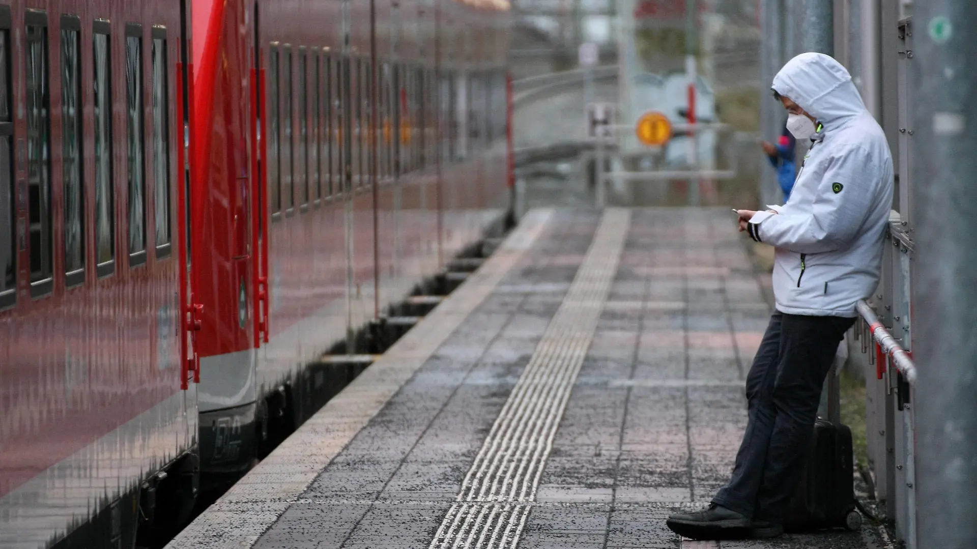 DB , Deutsch Bahn , Railway , Train , A young men with Safety Mask FFP2 and Mobile Phone is seen at Nurnberg Steinbuhl Station during the Hard Lockdown of the Covid 19 Coronavirus Pandemie in Nurnberg Nuremberg , Bayern , Deutschland . February 03 , 2021.