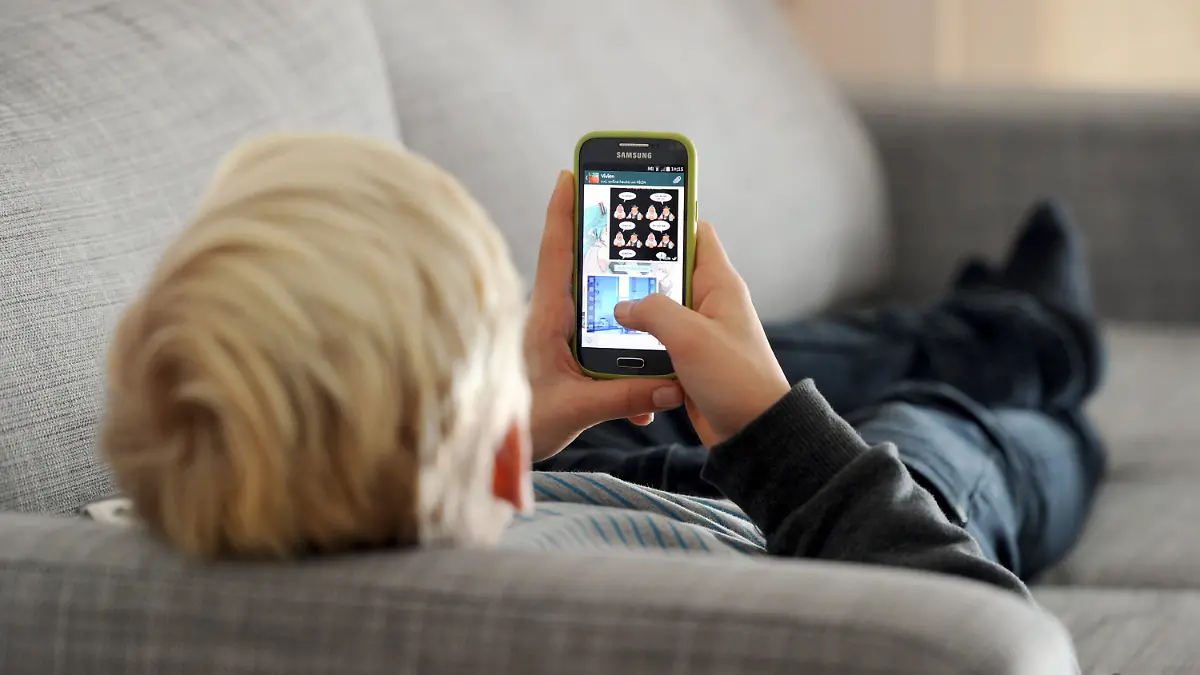 ARCHIV - 09.12.2014, Bayern, München: Ein Jugendlicher liegt auf einem Sofa und schaut auf sein Smartphone. Dauernd am Handy und mit Kettenbriefen, Mobbing oder Pornografie konfrontiert - die Mehrheit der Eltern berichtet von schlechten Erfahrungen ihrer Kids im Netz und fordert mehr gesetzlichen Schutz. Foto: Tobias Hase/dpa +++ dpa-Bildfunk +++