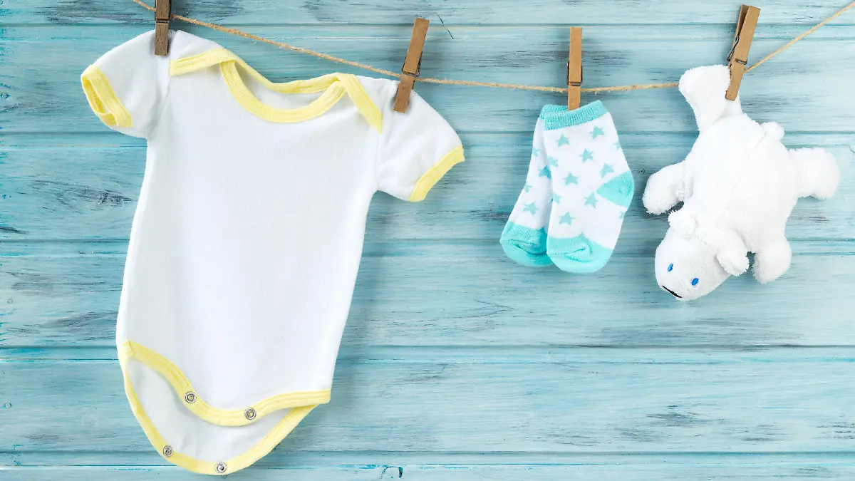 Baby clothes and white bear toy on a clothesline, wooden background