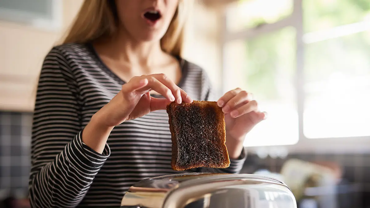 Shot of a woman removing a slice of burnt toast from a toaster at home