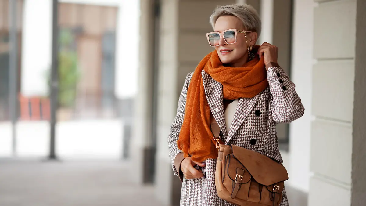 Smiling Woman Outdoor Portrait. Short blonde hair fashion model wears stylish clothes, double-breasted jacket, leather handbag, ochre knitted scarf and glasses. Fashion trend of autumn or spring