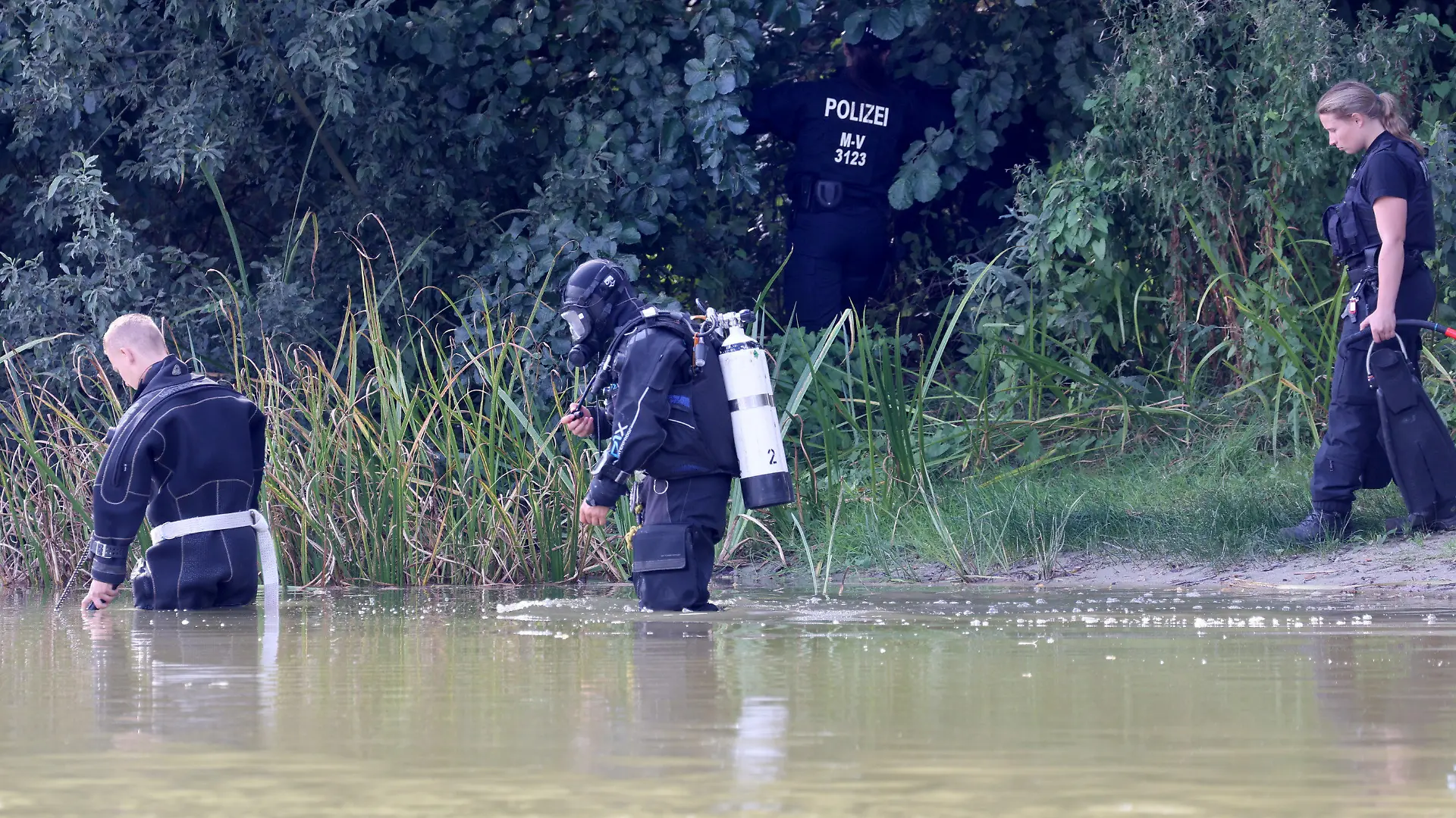 15.09.2023, Mecklenburg-Vorpommern, Pragsdorf: Polizisten, darunter ein Taucher, suchen im Uferbereich des Sees in Pragsdorf bei Neubrandenburg nach Tatgegenständen, wo am Abend des 14.09.2023 der schwer verletzte Sechsjährige gefunden wurde, der später an seinen Verletzungen verstarb. Die Polizei ermittelt wegen Totschlags. Foto: Bernd Wüstneck/dpa +++ dpa-Bildfunk +++