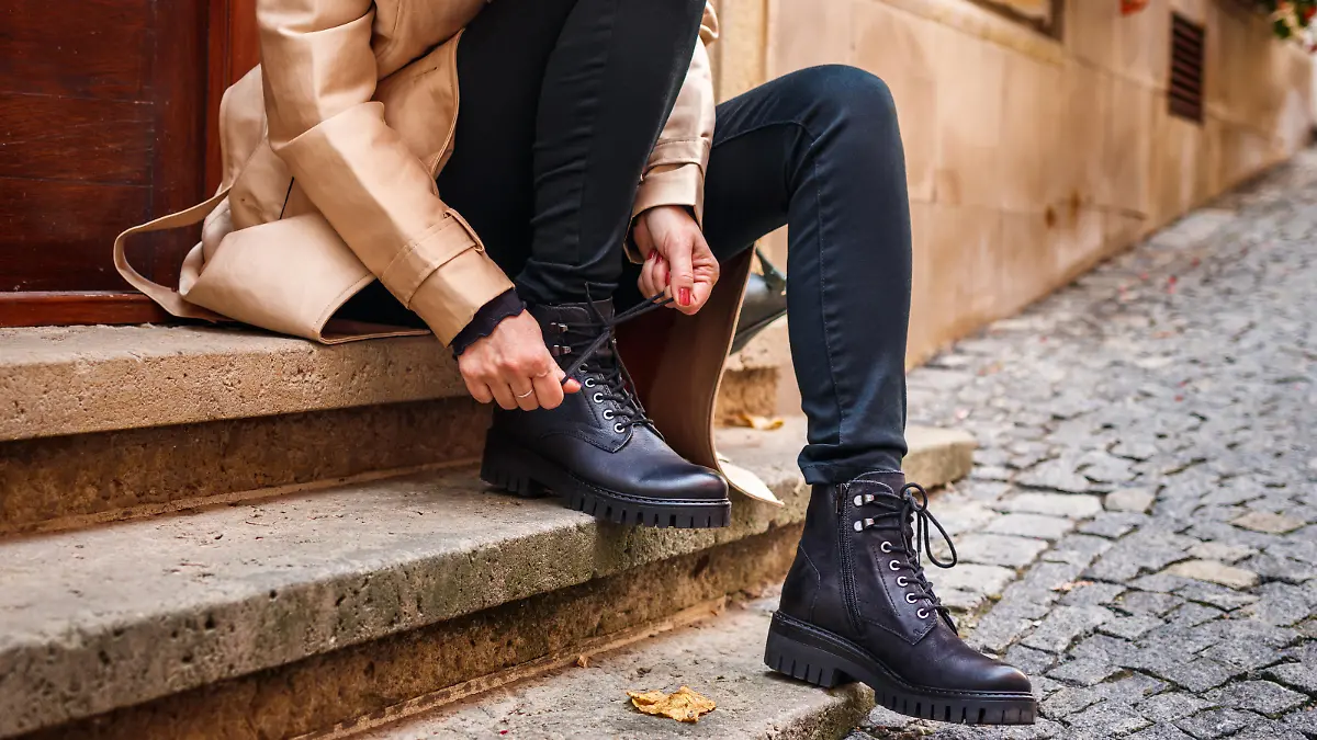 Frau sitzt auf einer Treppe und bindet sich ihre schwarzen Boots.