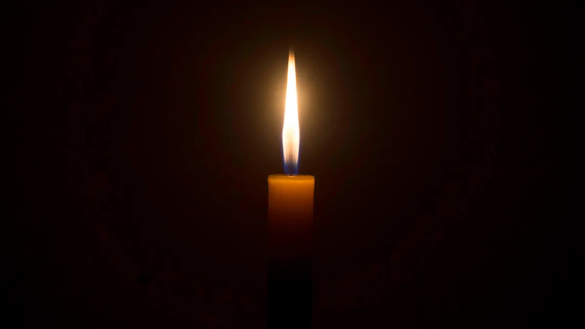 A single burning candle flame or light is glowing on an orange candle on black or dark background on table in church for Christmas, funeral or memorial service with copy space.