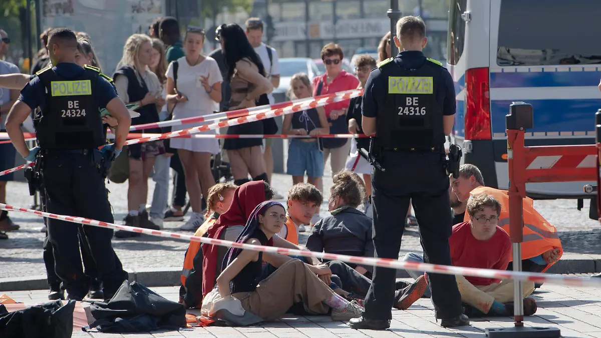 17.09.2023, Berln, Berlin: Polizeibeamte stehen am Brandenburger Tor um eine Gruppe festgesetzter Mitglieder der Klimaschutzgruppe Letzte Generation. Mitglieder der Klimaschutzgruppe Letzte Generation hatten am Sonntagvormittag das Brandenburger Tor mit oranger Farbe angesprüht. Die Polizei nahm nach eigenen Angaben 13 Mitglieder vor Ort fest. Foto: Paul Zinken/dpa +++ dpa-Bildfunk +++