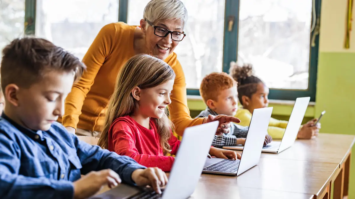 Happy mature teacher helping her students in using computers on a class at elementary school. Focus is on happy girl.