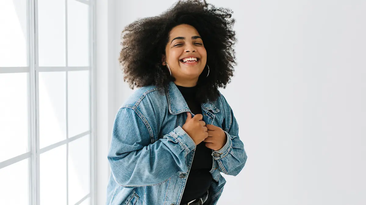 Beautiful woman wearing denim shirt over casual outfit standing near window. Pretty lady in fashionable clothing standing.