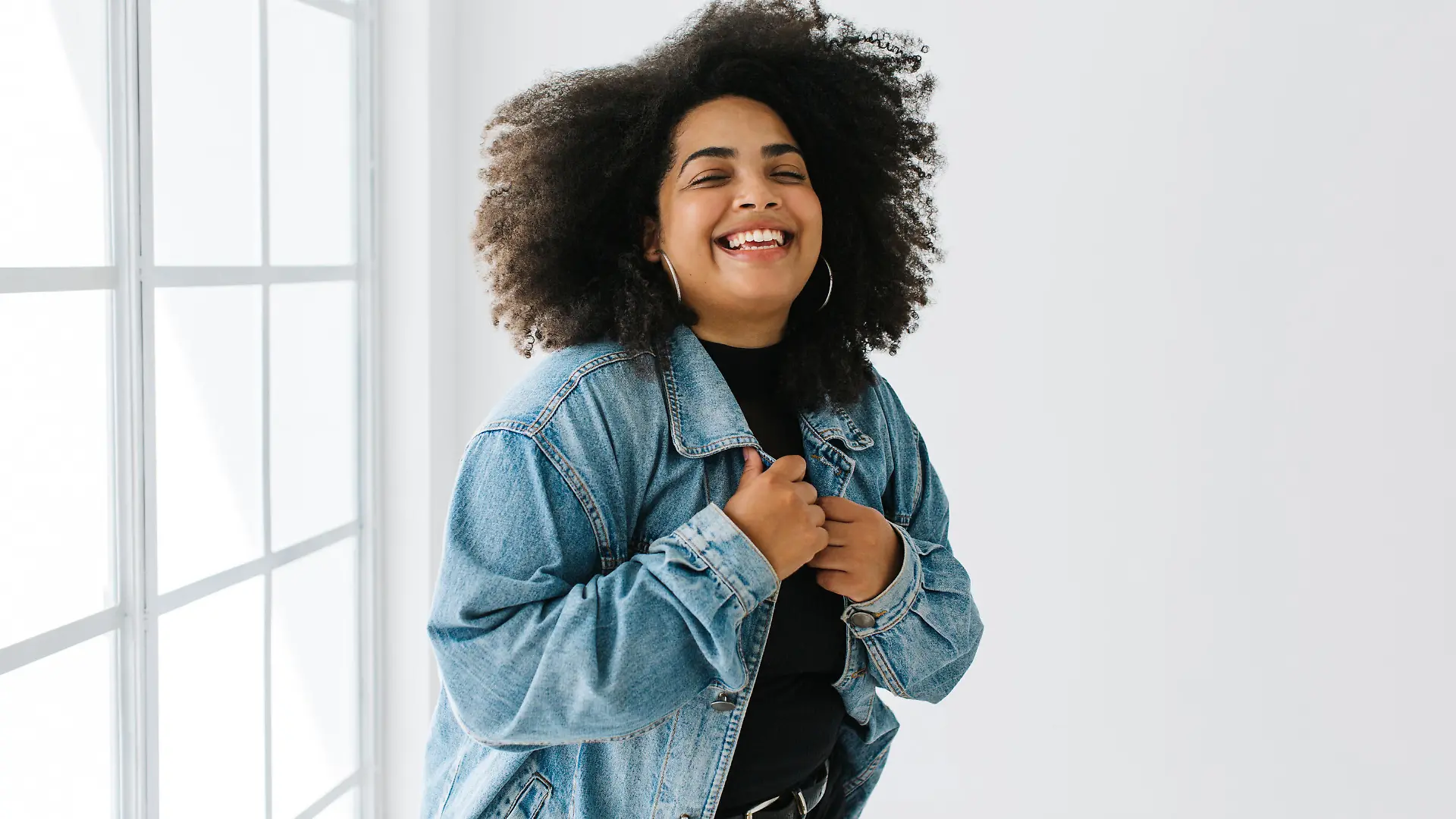 Beautiful woman wearing denim shirt over casual outfit standing near window. Pretty lady in fashionable clothing standing.