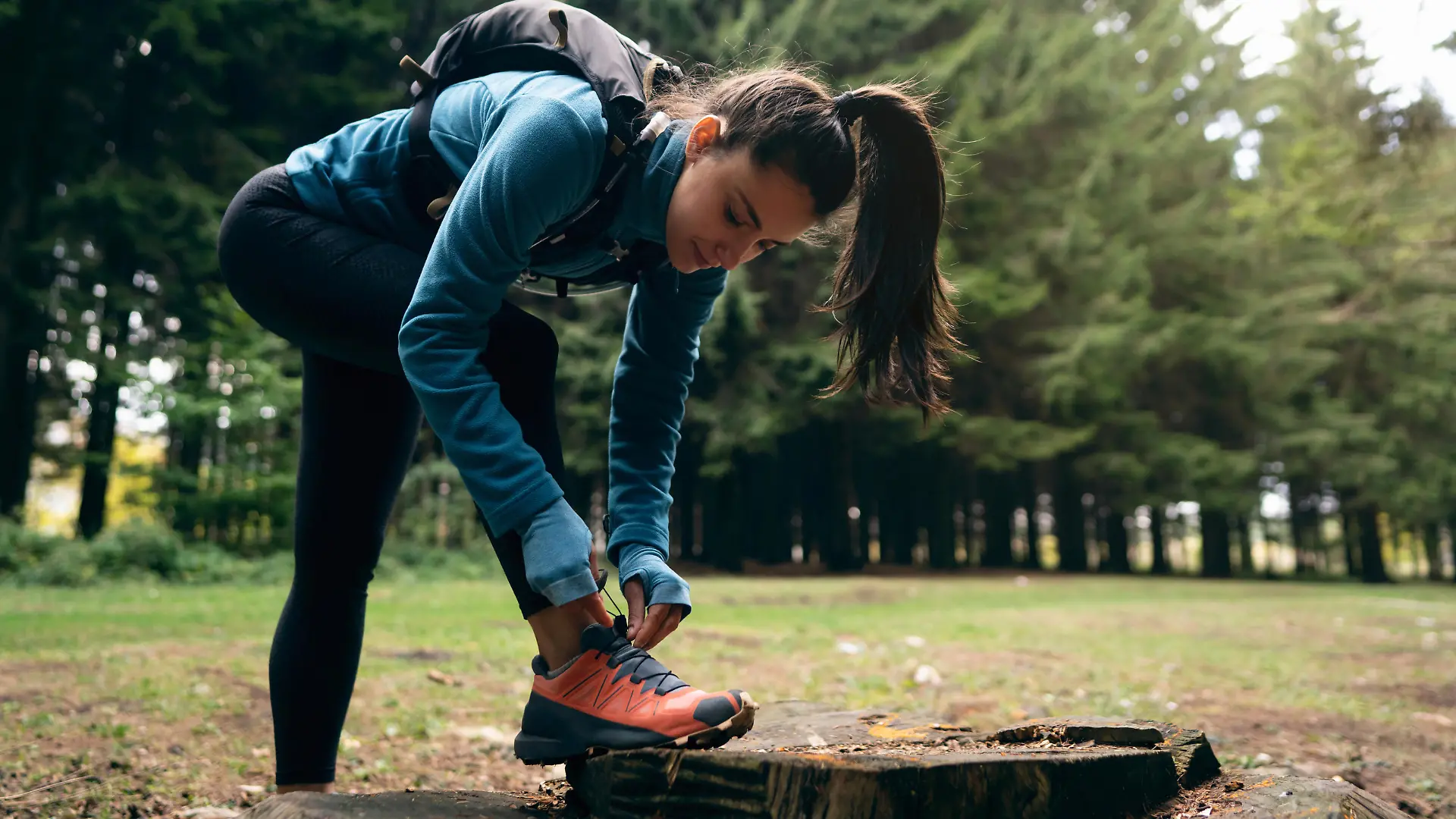 A Caucasian active and healthy young woman, tying her running sports shoe, during her hike in the forest