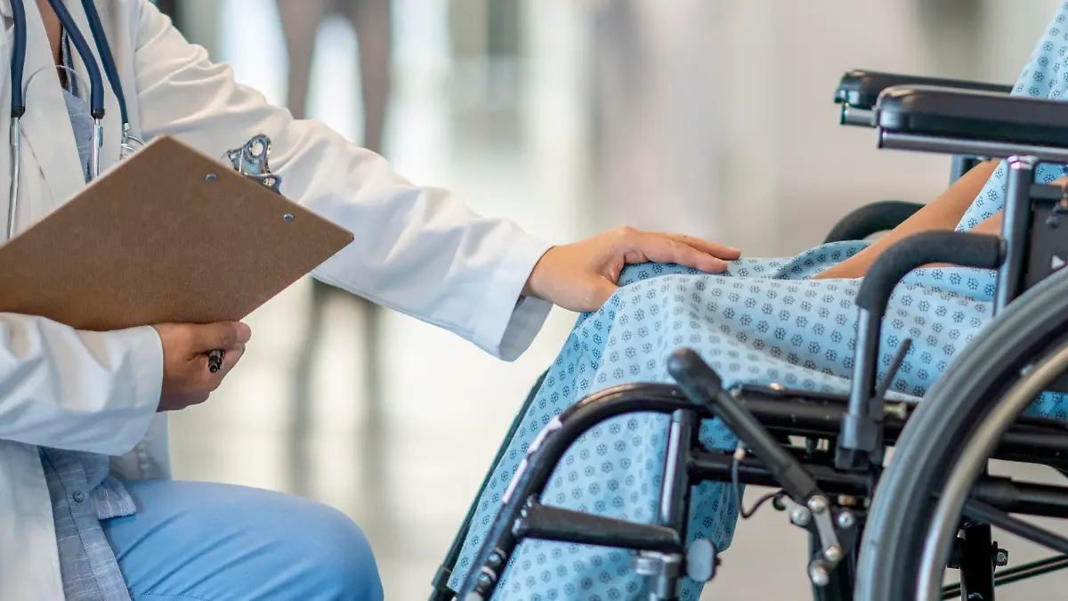 A teen girl with a disability sits in a wheelchair and is helped by a doctor who approaches her in an empathetic way.