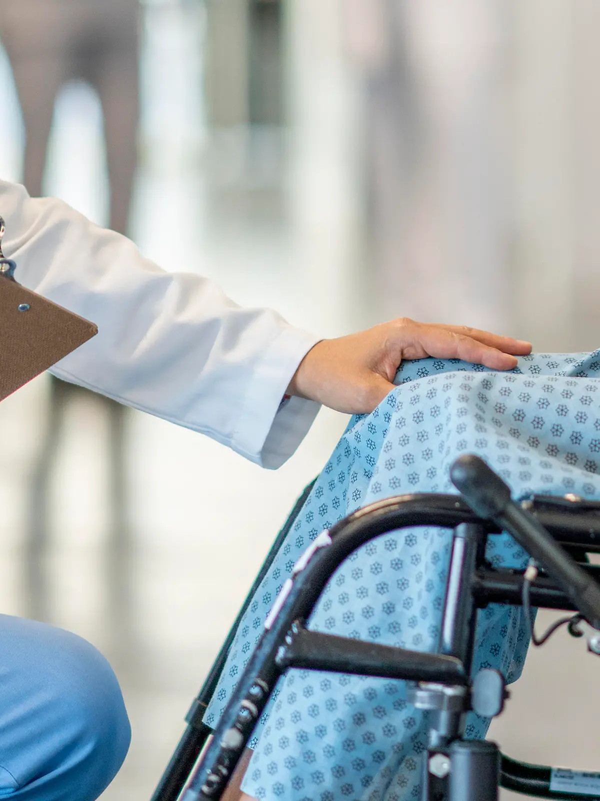 A teen girl with a disability sits in a wheelchair and is helped by a doctor who approaches her in an empathetic way.