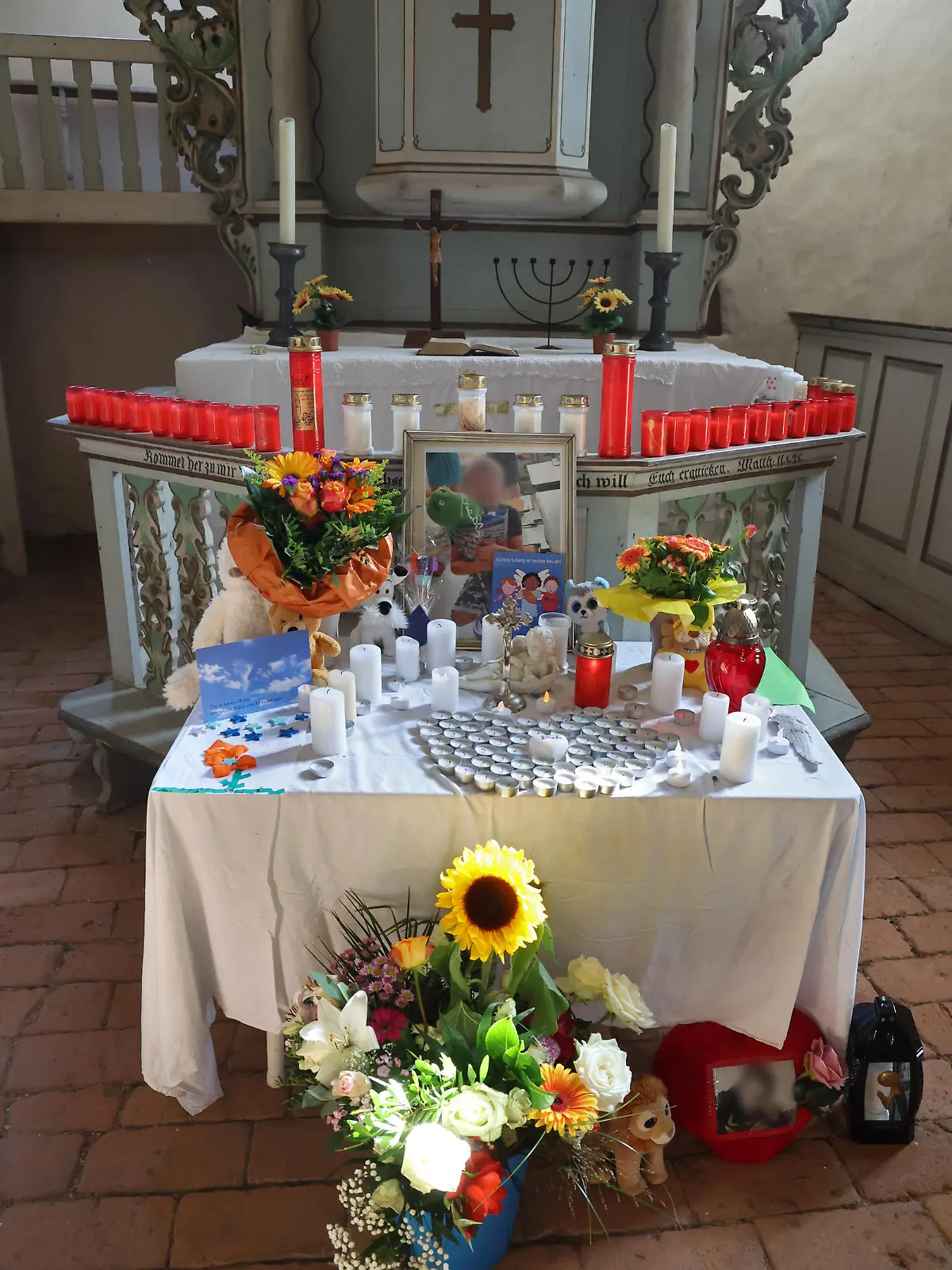 18.09.2023, Mecklenburg-Vorpommern, Pragsdorf: Auf dem Altar in der Kirche stehen Kerzen, Blumen und Fotos zum Gedenken an den Sechjährigen. Die Ermittlungenen nach der Tötung eines Sechsjährigen am See laufen nach wie vor auf Hochtouren. Foto: Bernd Wüstneck/dpa - ACHTUNG: Person(en) wurde(n) aus rechtlichen Gründen gepixelt +++ dpa-Bildfunk +++