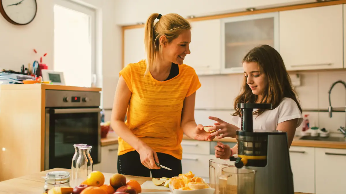 Mother and daughter making cold-pressed juice in the kitchen