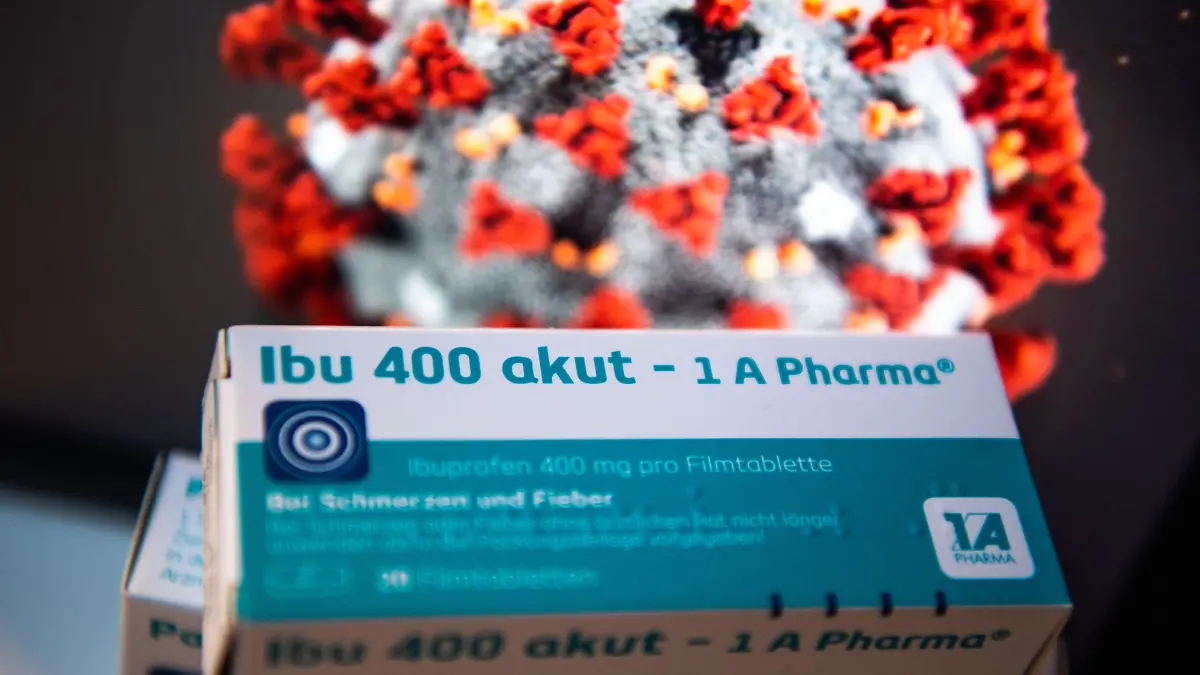 ILLUSTRATION - Eine Packung Ibuprofen liegt vor einer Abbildung des Coronavirus auf einem Tisch, die WHO hat vor der Einnahme von Ibuprofen bei einer Coronainfektion gewarnt.