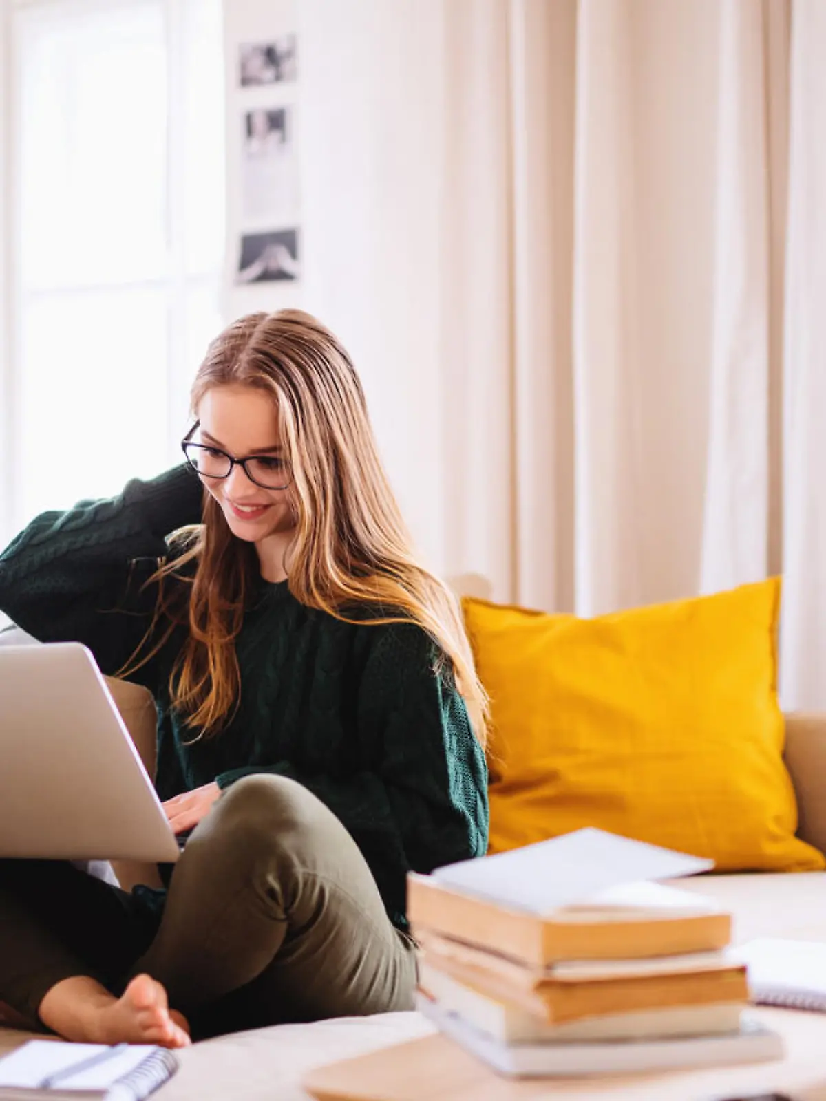 A young happy college female student sitting on sofa at home, using laptop when studying.