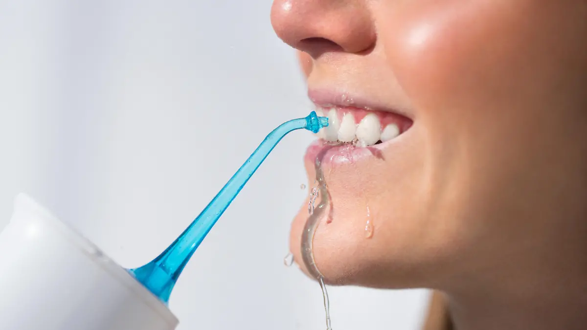 Woman with perfect white smile using portable water flosser or oral irrigator. High quality photo