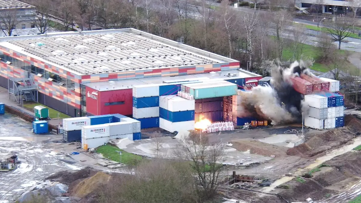 Eine Bombe wird kontrolliert gesprengt. Zwischen Containern steigt eine Rauchwolke auf.