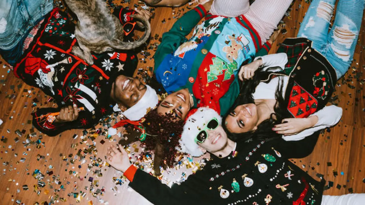 A group of young adult friends gather at a home for Christmas celebration over the holiday, dressed to fit the occasion with various Christmas accessories and ugly sweaters. They relax on the floor, covered with confetti.