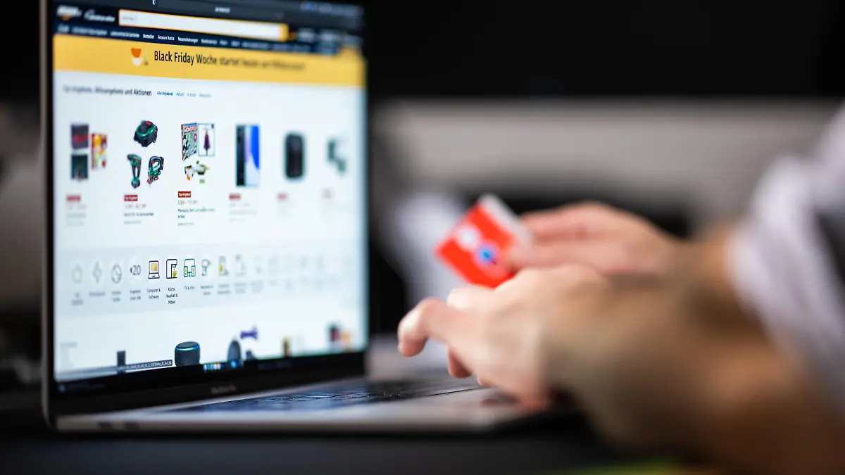 Ein Mann mit einer Bankkarte in der Hand sitzt am Laptop und schaut sich die Black Friday Angebote auf der Online-Shopping-Seite von Amazon an. (zu dpa „Trotz Lieferengpässen: Black Friday lockt Schnäppchenjäger“)