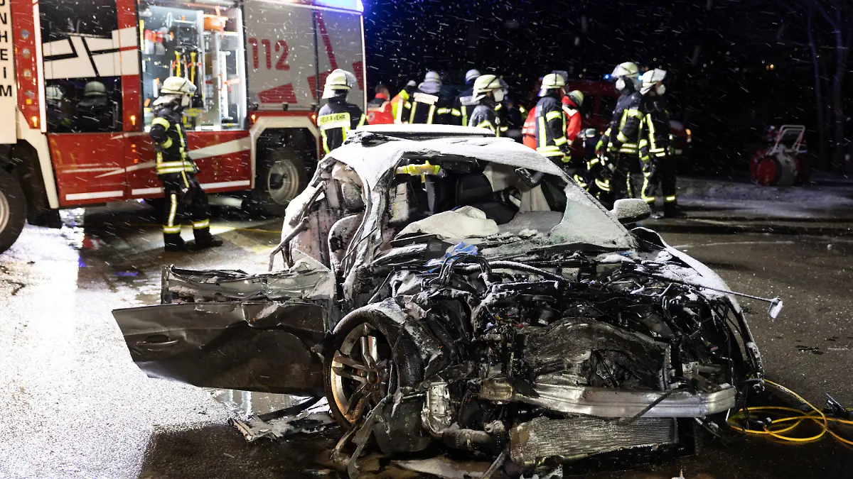 ARCHIV - 06.04.2021, Donau-Ries, Monheim: Feuerwehrleute stehen an einer Unfallstelle hinter einem Autowrack. Eine 54 Jahre alte Frau ist noch am Unfallort gestorben, nachdem ein Autofahrer frontal mit seinem Wagen in ihr Fahrzeug gefahren war. Der 28 Jahre alte Autofahrer muss sich wegen eines verbotenen Autorennens vor dem Landgericht Augsburg verantworten, nachdem er etwa doppelt so schnell wie erlaubt gefahren ist und die Kontrolle über seinen Wagen verloren hat. Am Donnerstag will das Gericht das Urteil verkünden. (zu dpa «Gericht verkündet nach tödlichem Raserunfall Urteil») Foto: Ralph Goppelt/vifogra/dpa +++ dpa-Bildfunk +++