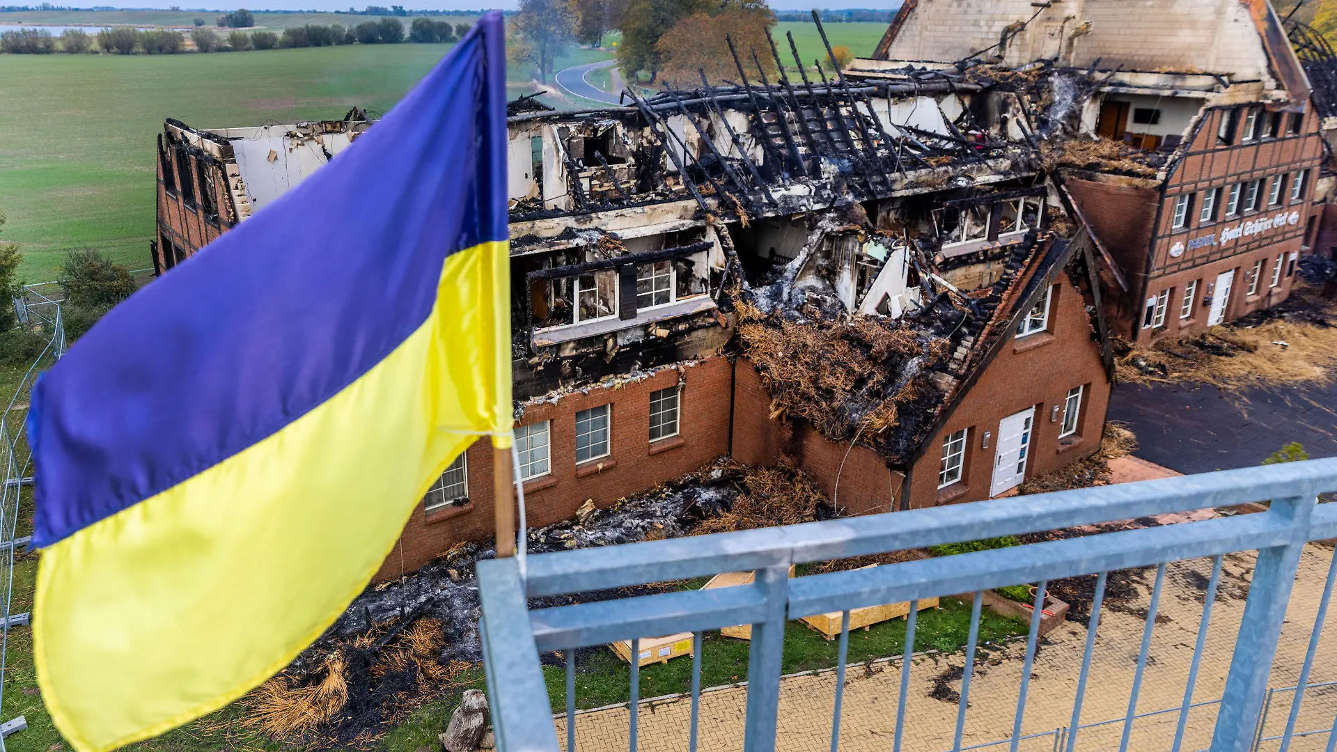 21.10.2022, Mecklenburg-Vorpommern, Groß Strömkendorf: Die ukrainische Fahne weht auf dem Dach eines Nebengebäudes vor den Resten des abgebrannten Hotelgebäudes. Das Gebäude in dem Flüchtlinge aus der Ukraine untergebracht waren, ist in der Nacht vom 19. zum 20.10.2022 komplett abgebrannt. Verletzt wurde bei dem Feuer niemand, vermutet wird Brandstiftung. Die 14 Bewohner wurden nach den Rettungsarbeiten in anderen Wohnungen untergebracht. Foto: Jens Büttner/dpa +++ dpa-Bildfunk +++