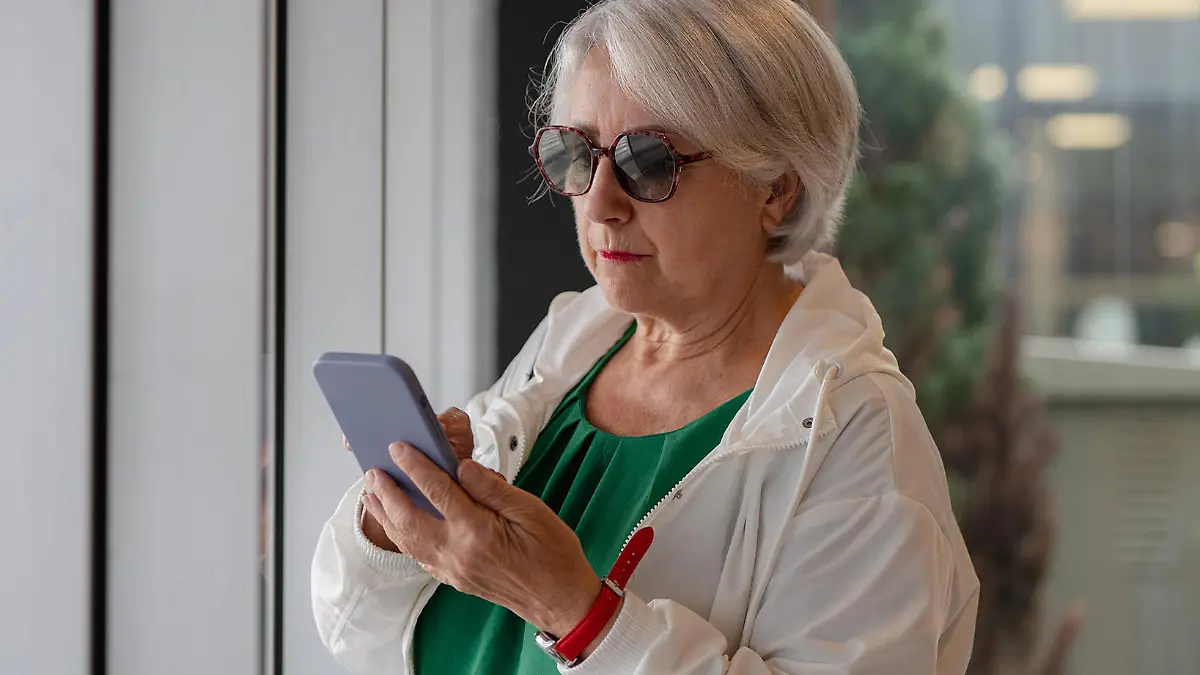 MR_ID14379_13537_MariasunMuNoz.jpg Focused aged lady with short gray hair in sunglasses surfing internet on smartphone while standing near window, Model released HodeiUnzueta_ID14379_431670_004 Copyright: xHodeixUnzuetax