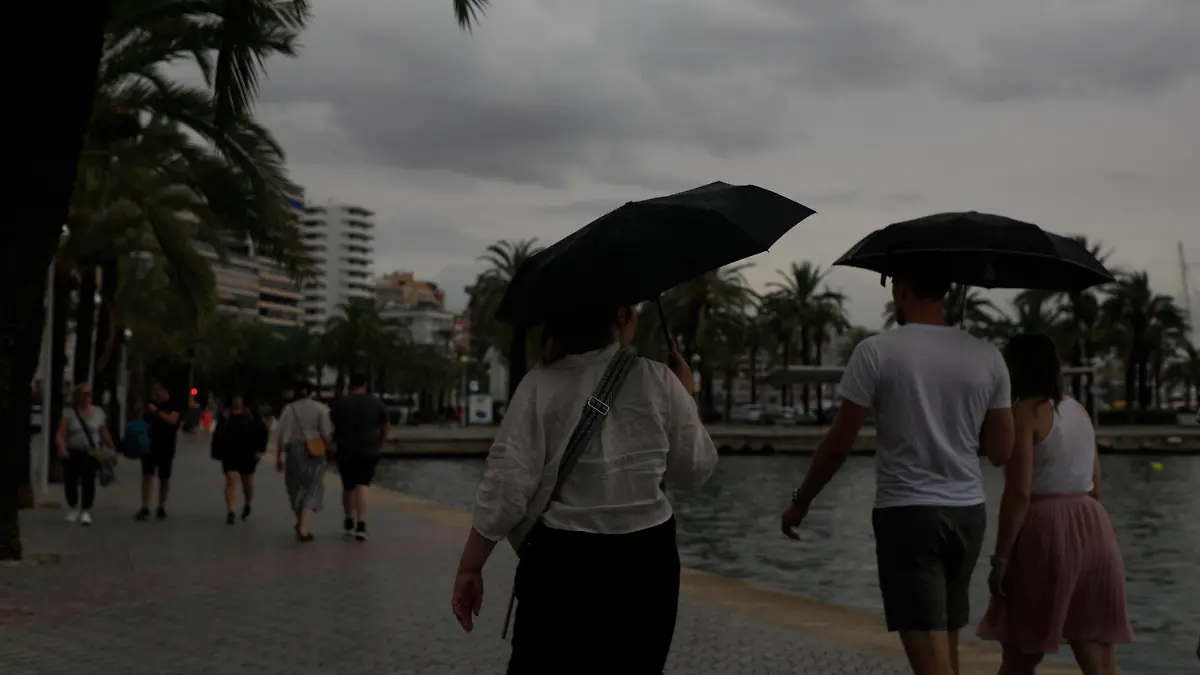 02.09.2023, Spanien, Palma: Mit Schirmen sind Spaziergänger an der Strandpromenade unterwegs. Auf Mallorca wurde wegen möglicher Unwetter die gelbe Alarmstufe ausgerufen. Foto: Clara Margais/dpa +++ dpa-Bildfunk +++
