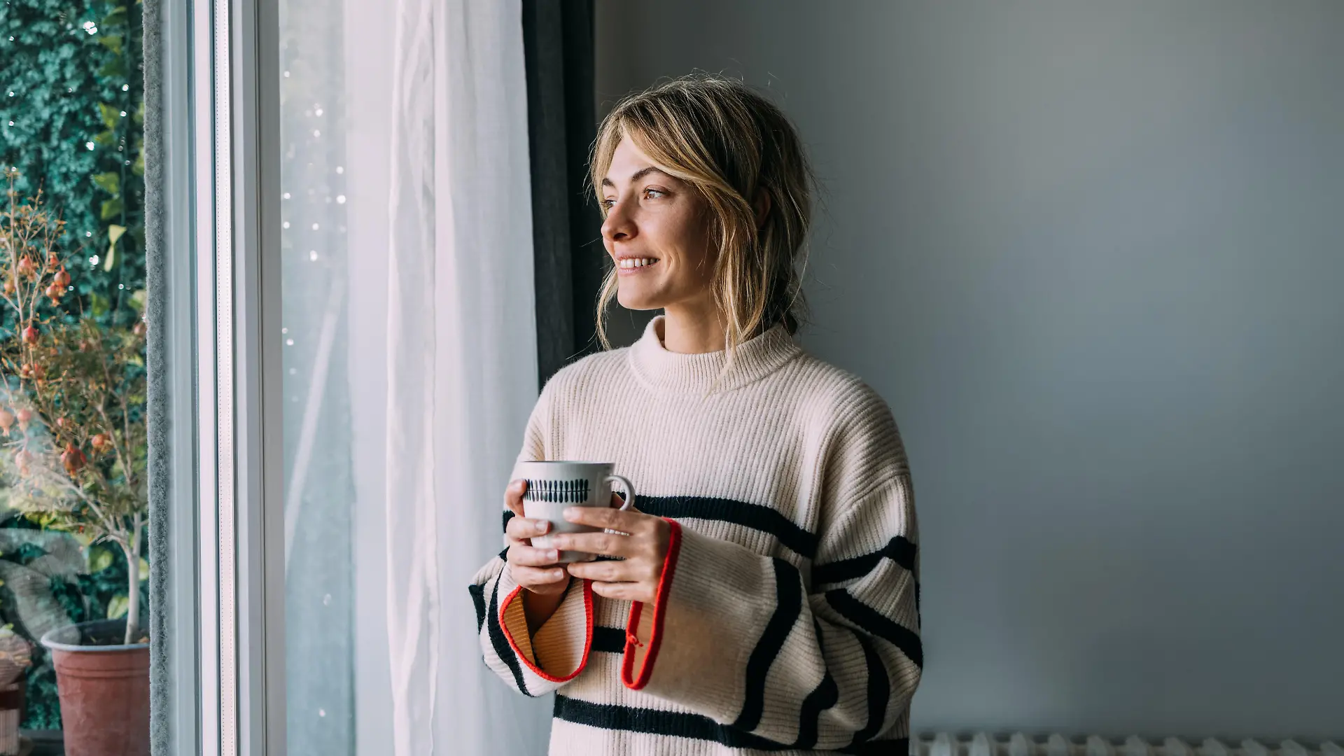 Optimistic mornings: a smiling young woman drinking tea by the window.