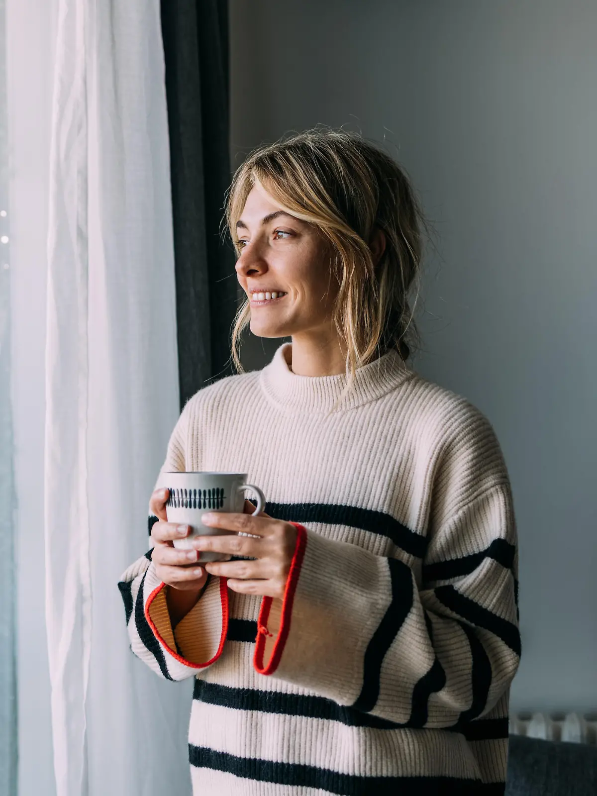 Optimistic mornings: a smiling young woman drinking tea by the window.
