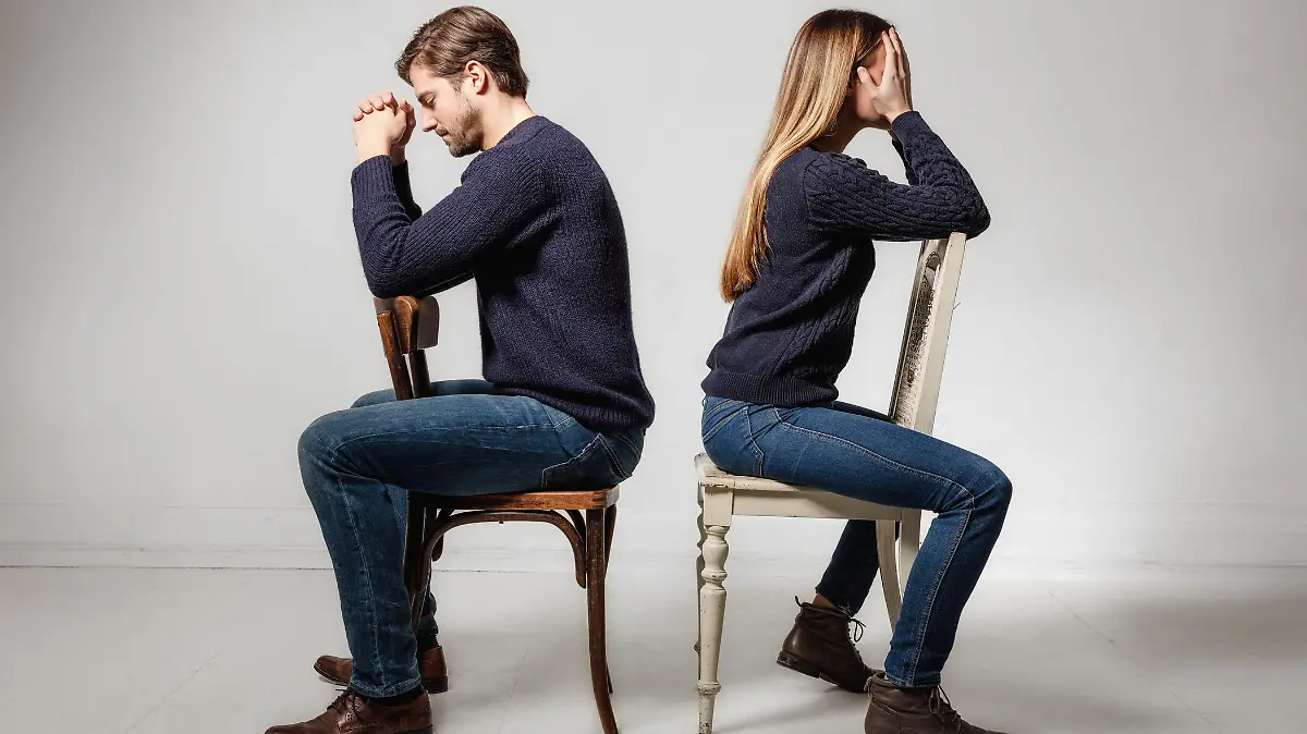 Side view of depressed couple sitting back to back on chairs against gray background
