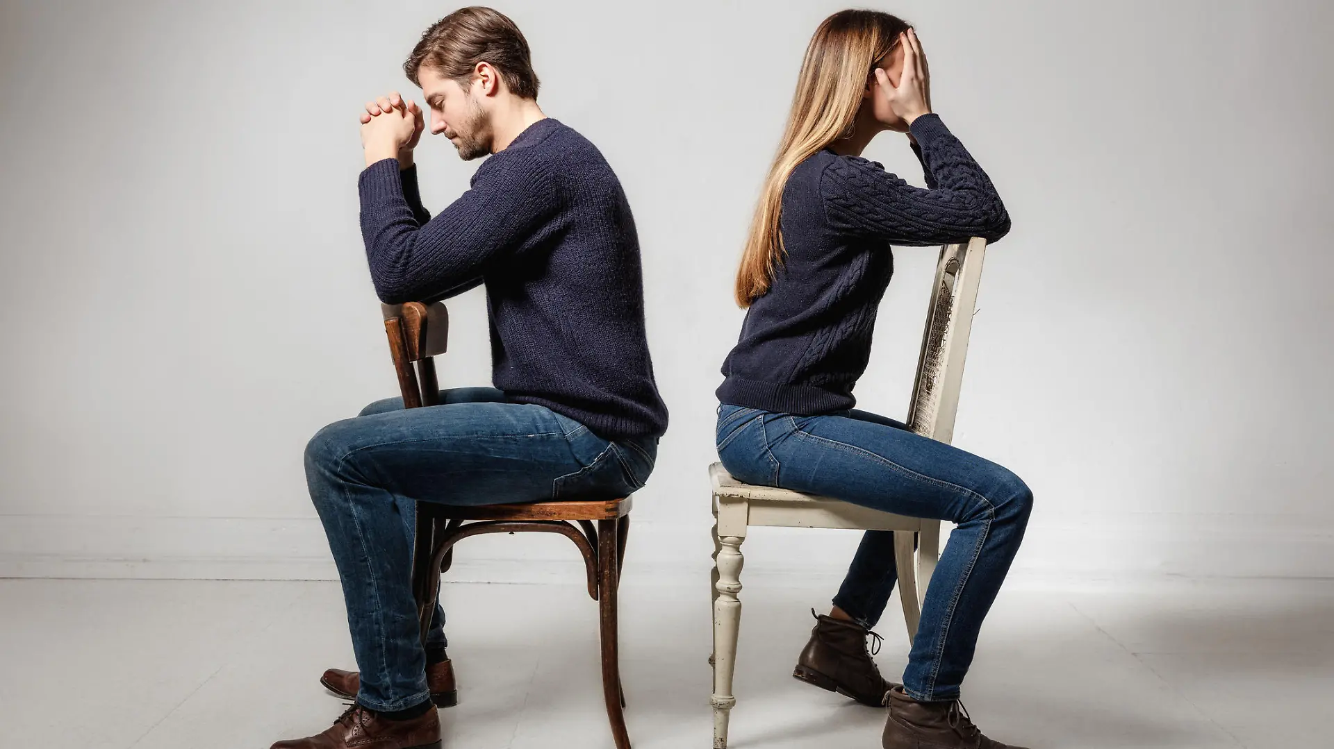 Side view of depressed couple sitting back to back on chairs against gray background