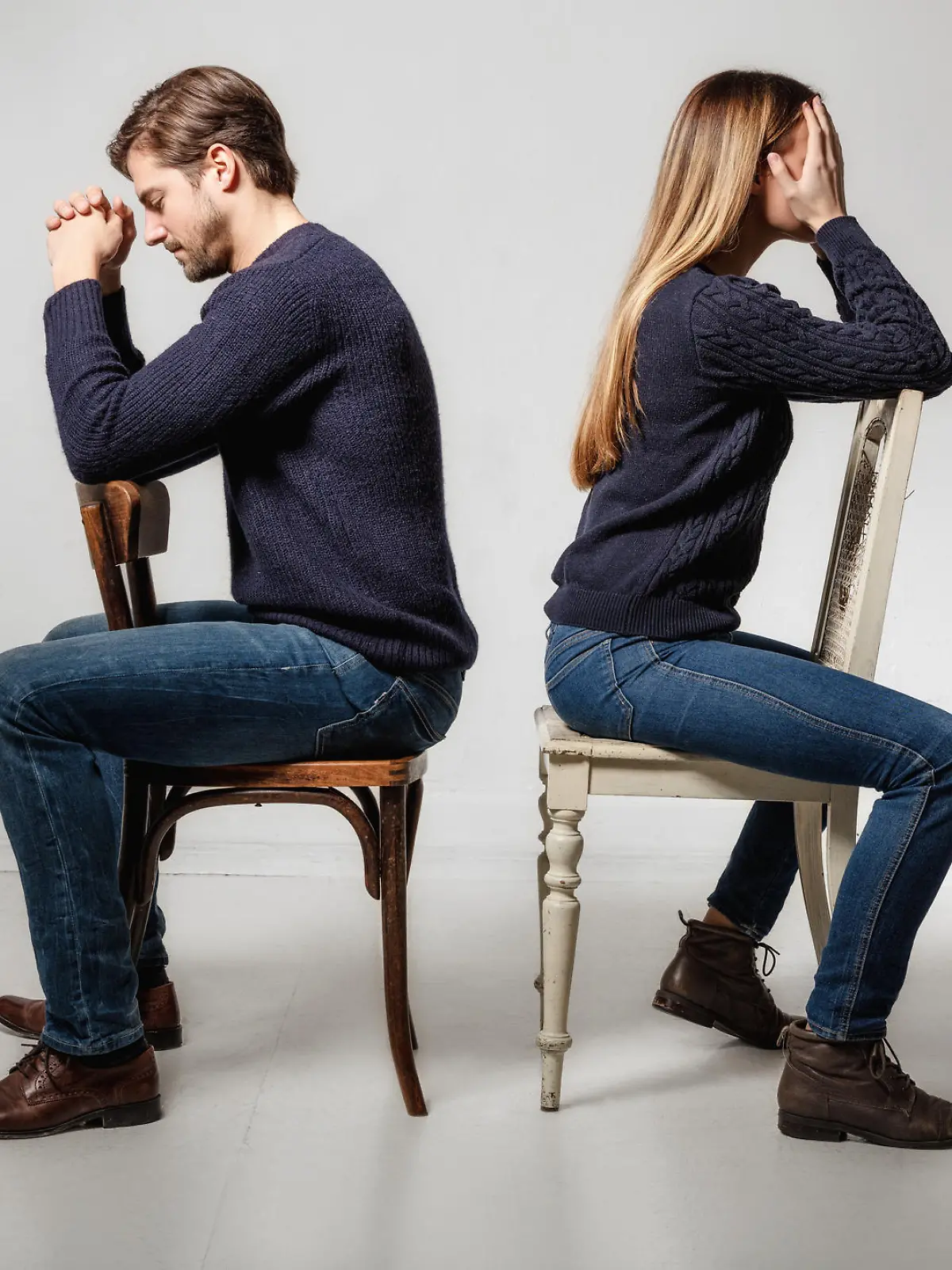 Side view of depressed couple sitting back to back on chairs against gray background