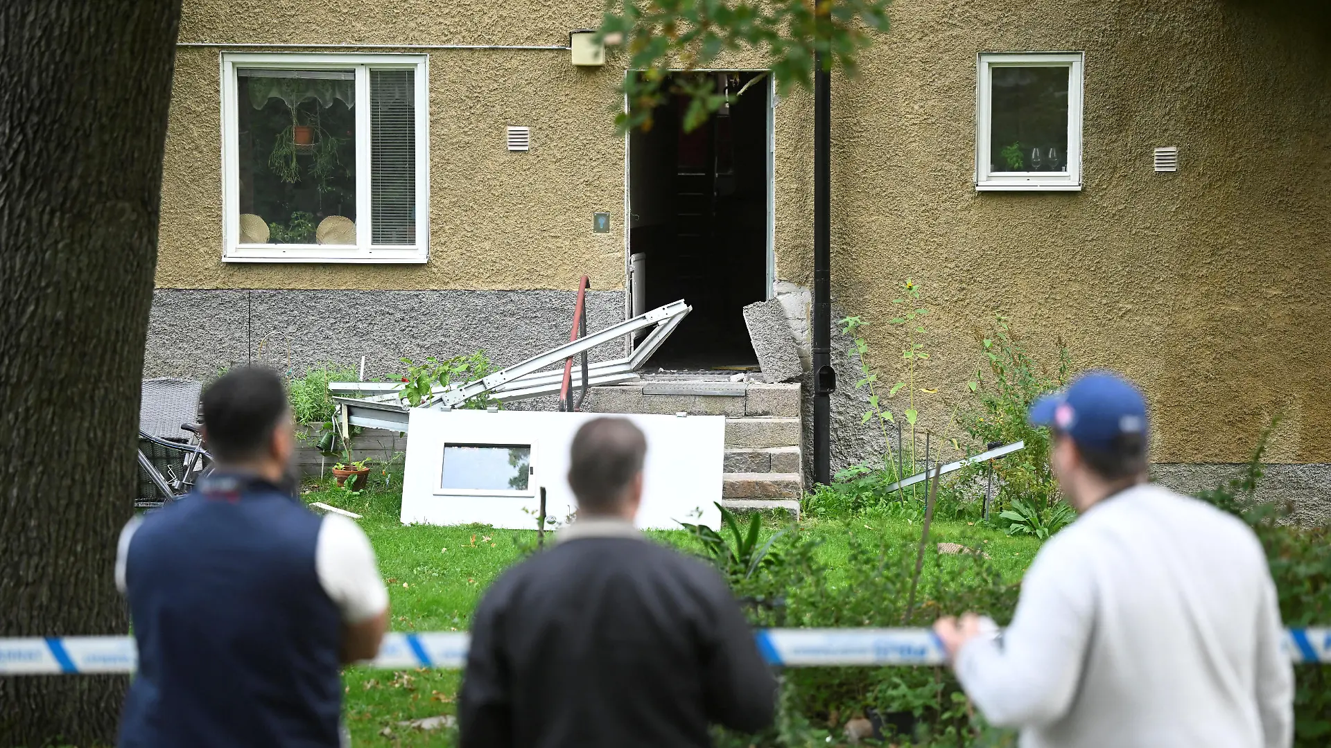 People stand outside a cordoned-off building with a damaged entrance following an explosion in Hasselby, Stockholm, Sweden, September 26, 2023. Fredrik Sandberg/TT News Agency/via REUTERS ATTENTION EDITORS - THIS IMAGE WAS PROVIDED BY A THIRD PARTY. SWEDEN OUT. NO COMMERCIAL OR EDITORIAL SALES IN SWEDEN.