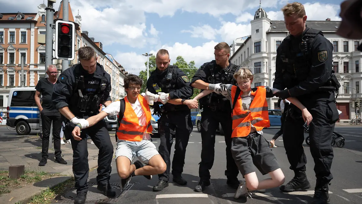 04.07.2023, Sachsen, Leipzig: Polizeibeamte heben zwei Klimaaktivisten der Gruppe «Letzte Generation» von einer Straße. Nur wenige Minuten nach dem Freispruch für fünf Mitglieder der «Letzten Generation» vom Vorwurf der Nötigung haben die Klimaaktivisten eine Hauptverkehrsstraße blockiert. Zehn Frauen und Männer setzten sich auf eine Kreuzung und protestierten gegen die Folgen der Klimakrise. Foto: Hendrik Schmidt/dpa +++ dpa-Bildfunk +++