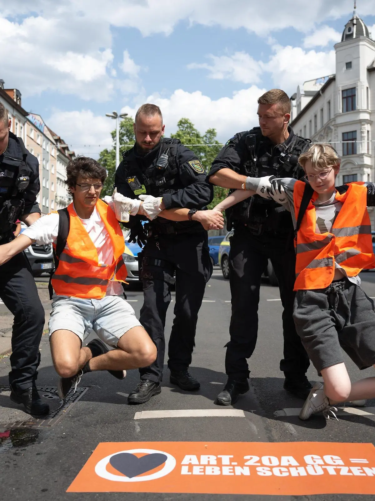 04.07.2023, Sachsen, Leipzig: Polizeibeamte heben zwei Klimaaktivisten der Gruppe «Letzte Generation» von einer Straße. Nur wenige Minuten nach dem Freispruch für fünf Mitglieder der «Letzten Generation» vom Vorwurf der Nötigung haben die Klimaaktivisten eine Hauptverkehrsstraße blockiert. Zehn Frauen und Männer setzten sich auf eine Kreuzung und protestierten gegen die Folgen der Klimakrise. Foto: Hendrik Schmidt/dpa +++ dpa-Bildfunk +++