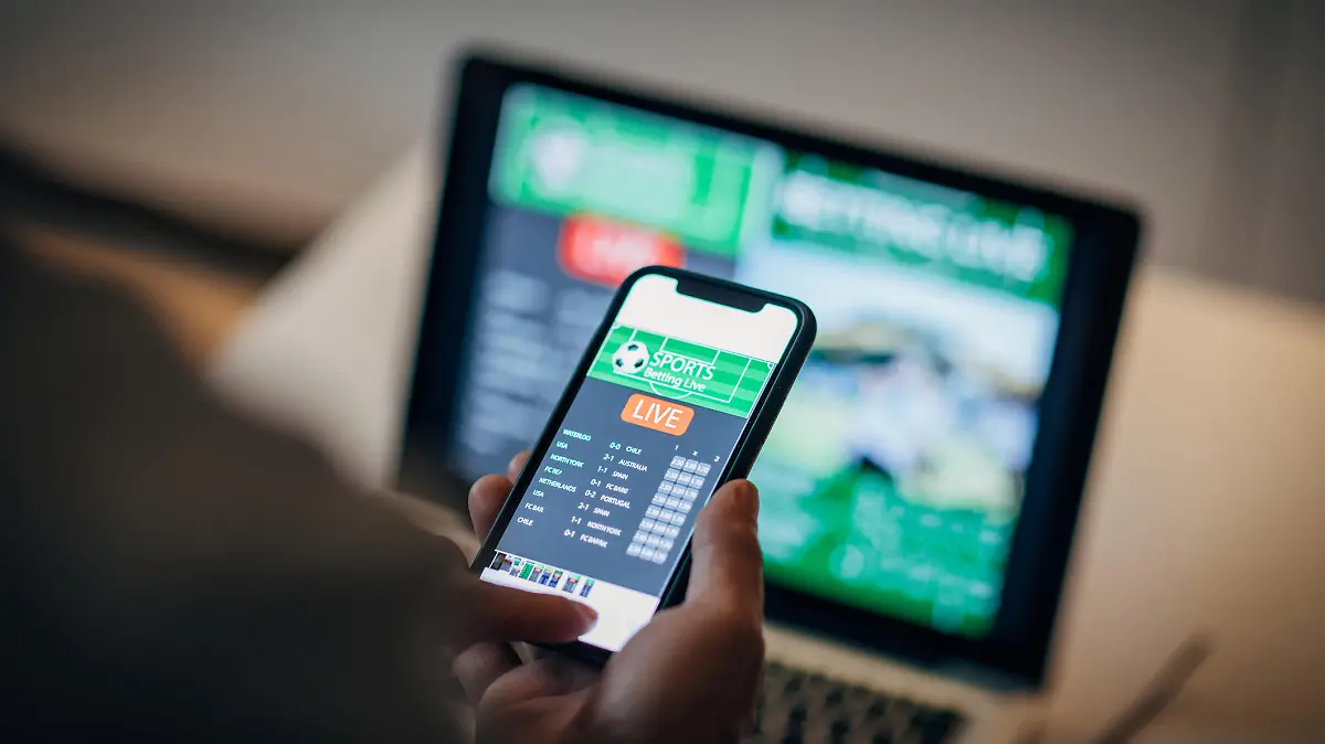 Mature man using mobile app for live betting and online gambling and watching a sports match