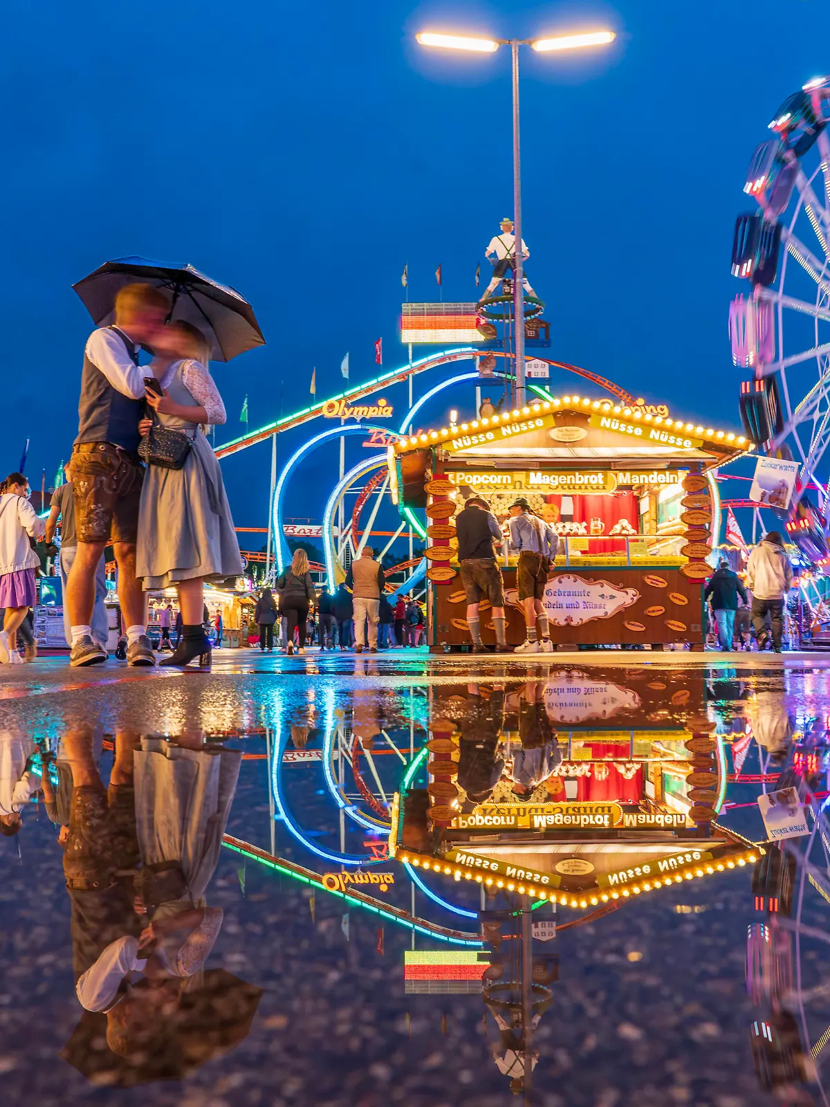 Wiesn im Regen, Lichter der Fahrgeschäfte leuchten in den Abendhimmel, spiegeln sich im Asphalt, München, 22.09.2023 Deutschland, München, 22.09.2023, Wiesn im Regen, Freitagabend, Lichter der Fahrgeschäfte spiegeln sich im nassen Asphalt, Wiesnbesucher unter Regenschirmen, in der Blauen Stunde, abends nach 19 Uhr, ein Paar küsst sich, Abendhimmel, Wiesn, Wochenende, Volksfest, Bayern, *** Wiesn in the rain, lights of the rides shine in the evening sky, reflected in the asphalt, Munich, 22 09 2023 Germany, Munich, 22 09 2023, Wiesn in the rain, Friday evening, lights of the rides reflected in the wet asphalt, Wiesn visitors under umbrellas, in the blue hour, evening after 7 pm, a couple kissing, evening sky, Wiesn, weekend, folk festiv