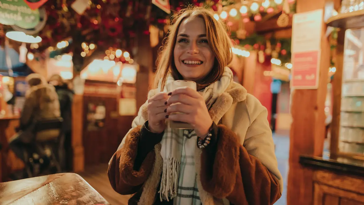 Portrait of a beautiful young smiling woman drinking mulled wine outdoors in the city street in Germany on a lovely winter night