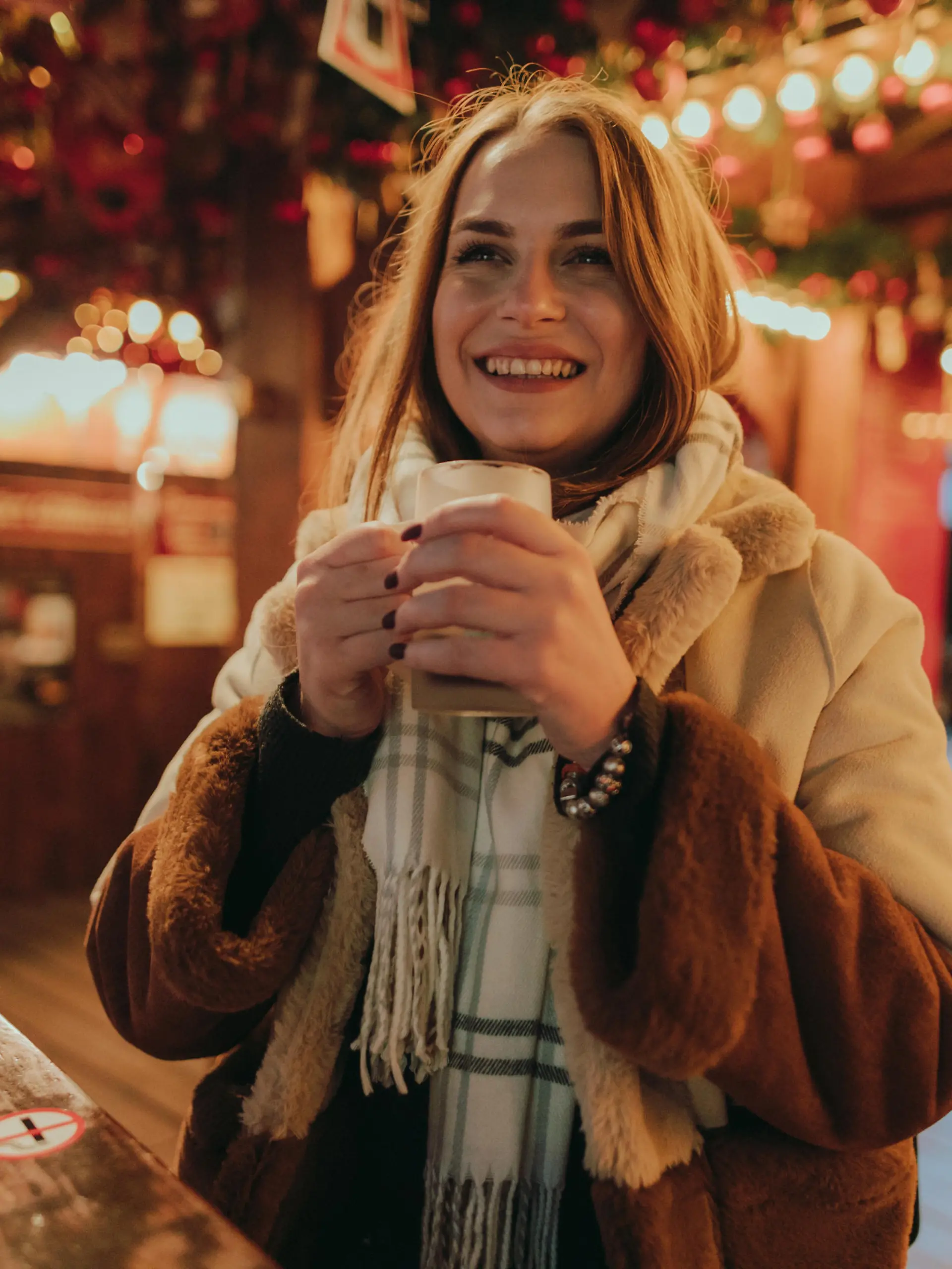 Portrait of a beautiful young smiling woman drinking mulled wine outdoors in the city street in Germany on a lovely winter night