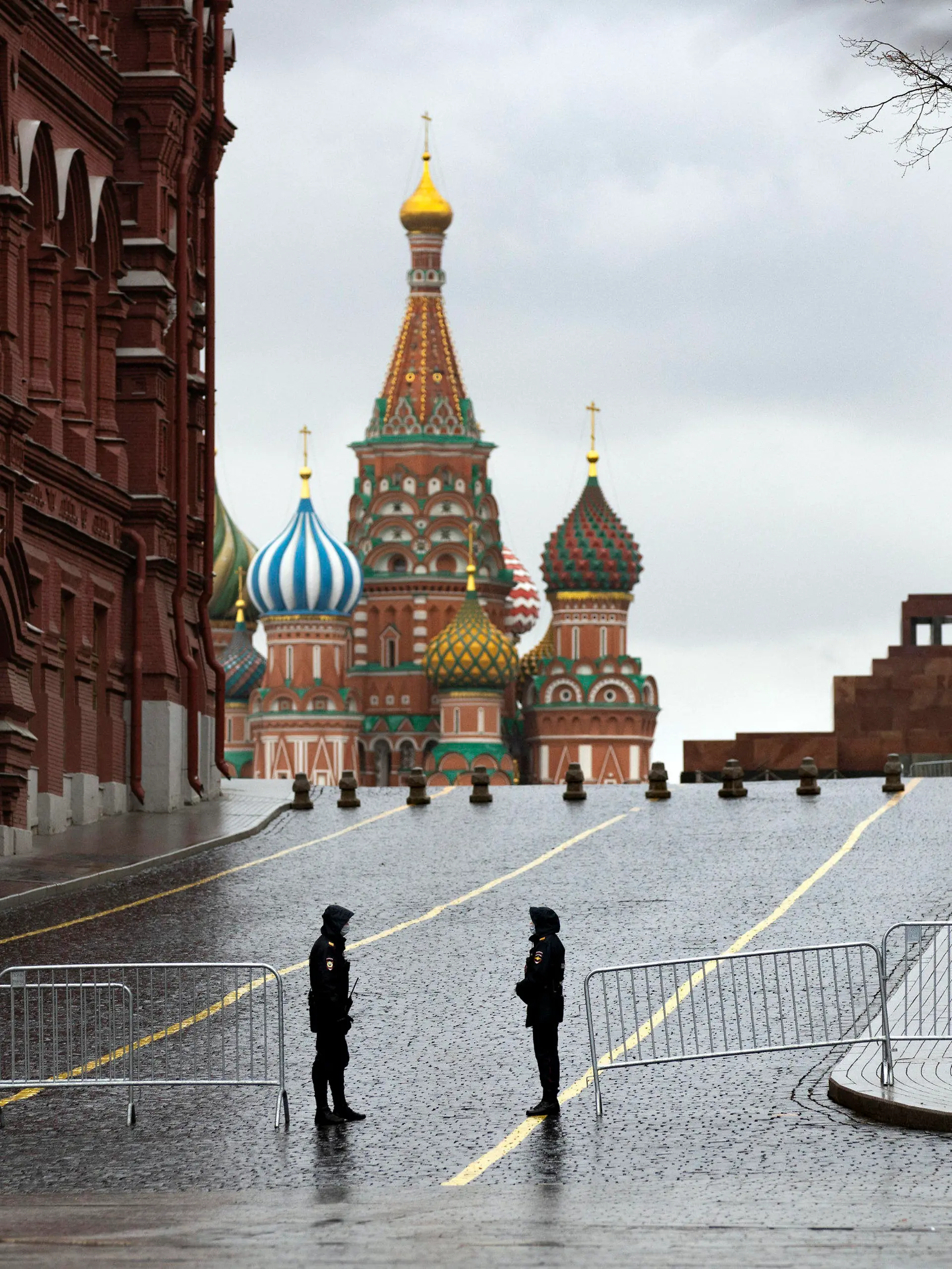 14.04.2020, Russland, Moskau: Zwei Polizisten mit Mundschutz bewachen bei Regen einen gesperrten Zugang auf dem leeren Roten Platz zur Einhaltung der Vorschriften zur Eindämmung des Coronavirus. Foto: Alexander Zemlianichenko/AP/dpa +++ dpa-Bildfunk +++