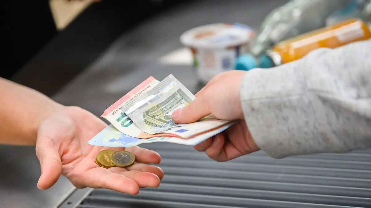 Eine Kassiererin reicht einer Kundin Wechselgeld an der Kasse eines Supermarkts.